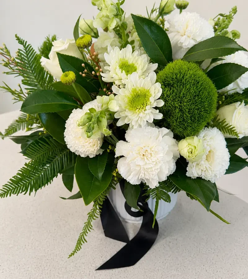 White and green ceramic vase arrangement with seasonal flowers and fresh foliage.