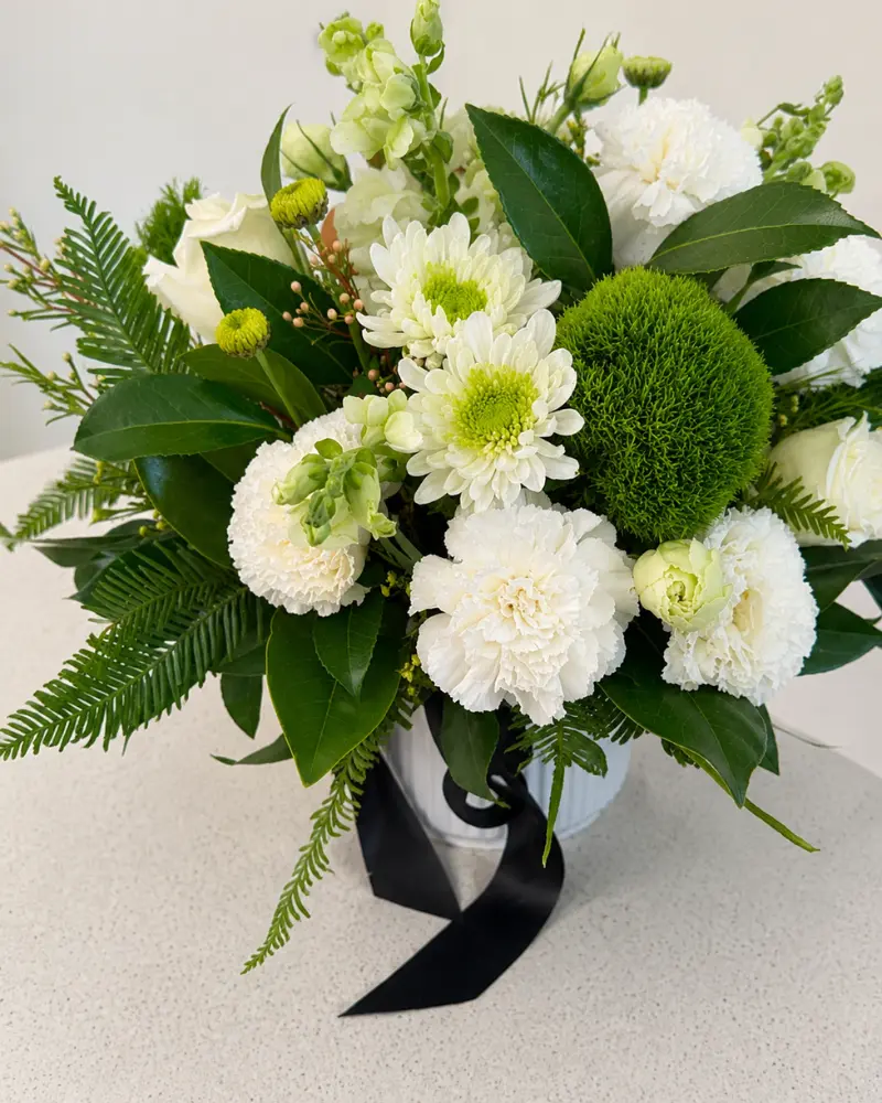 White and green ceramic vase arrangement with seasonal flowers and fresh foliage.