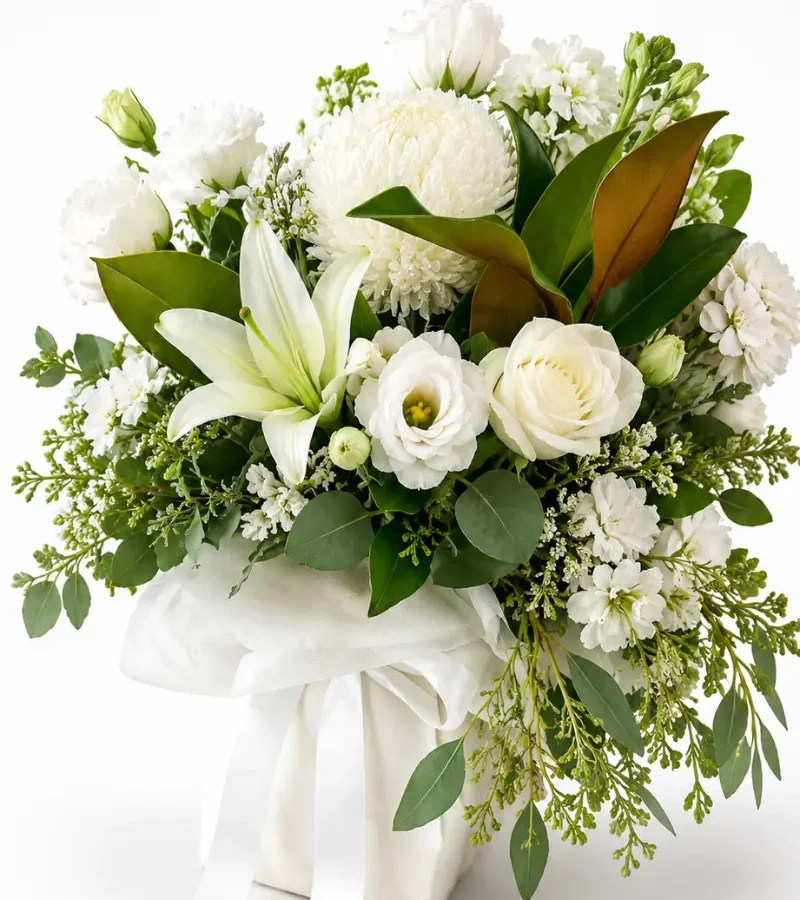 Classic white and green sympathy arrangement featuring white lilies, roses, lisianthus and seasonal foliage.