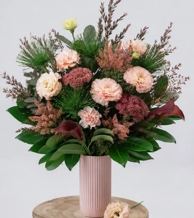 Pink and burgundy floral arrangement in a blush vase with lisianthus, calla lilies, native foliage, and greenery.