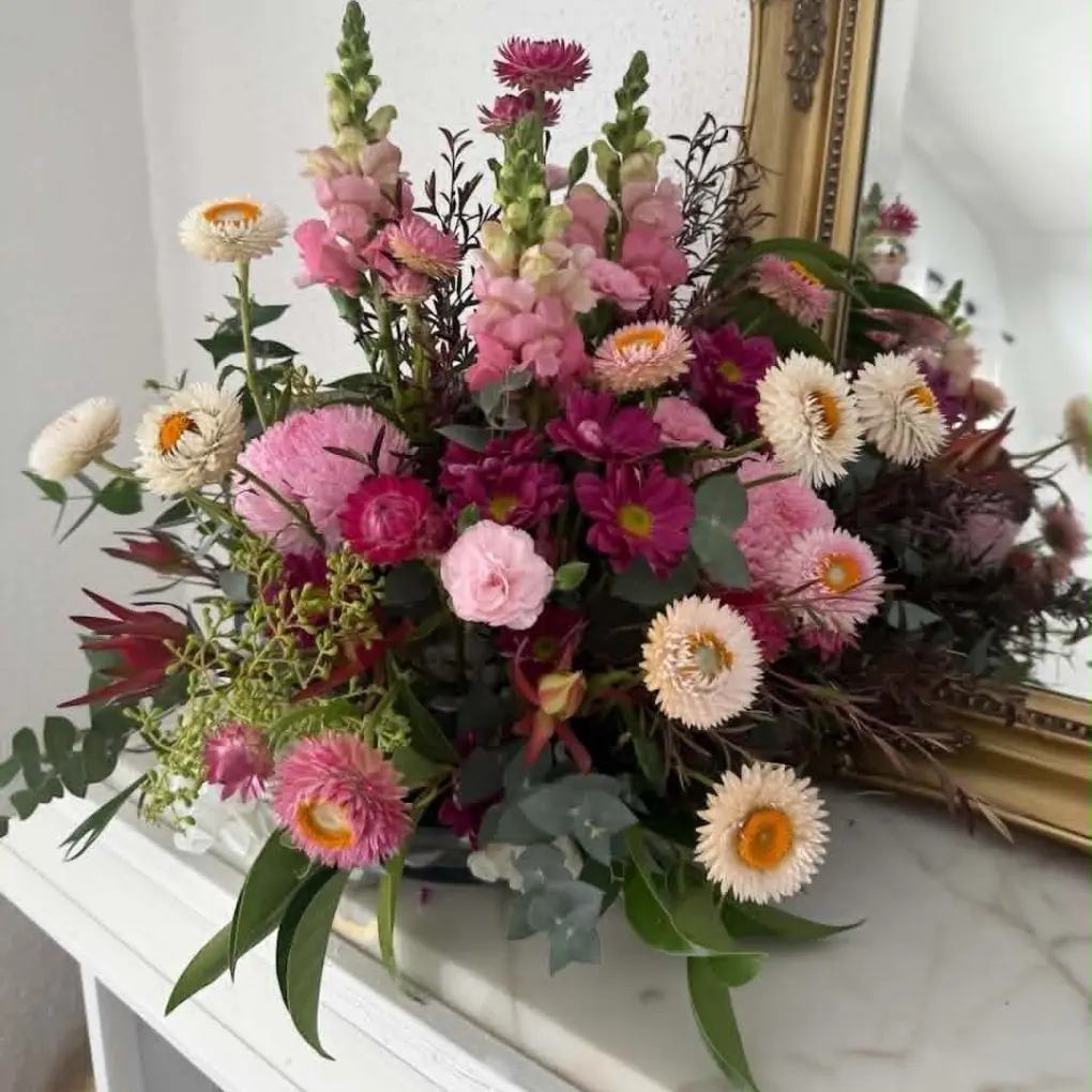 corporate-flowers Pink and burgundy floral arrangement styled on a console table beside a gold mirror in a corporate or office space.