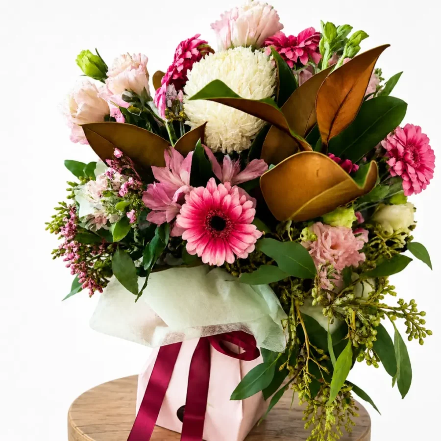 Pink flower gift vox arrangement with seasonal blooms, greenery and ribbon in a self-contained pink container.