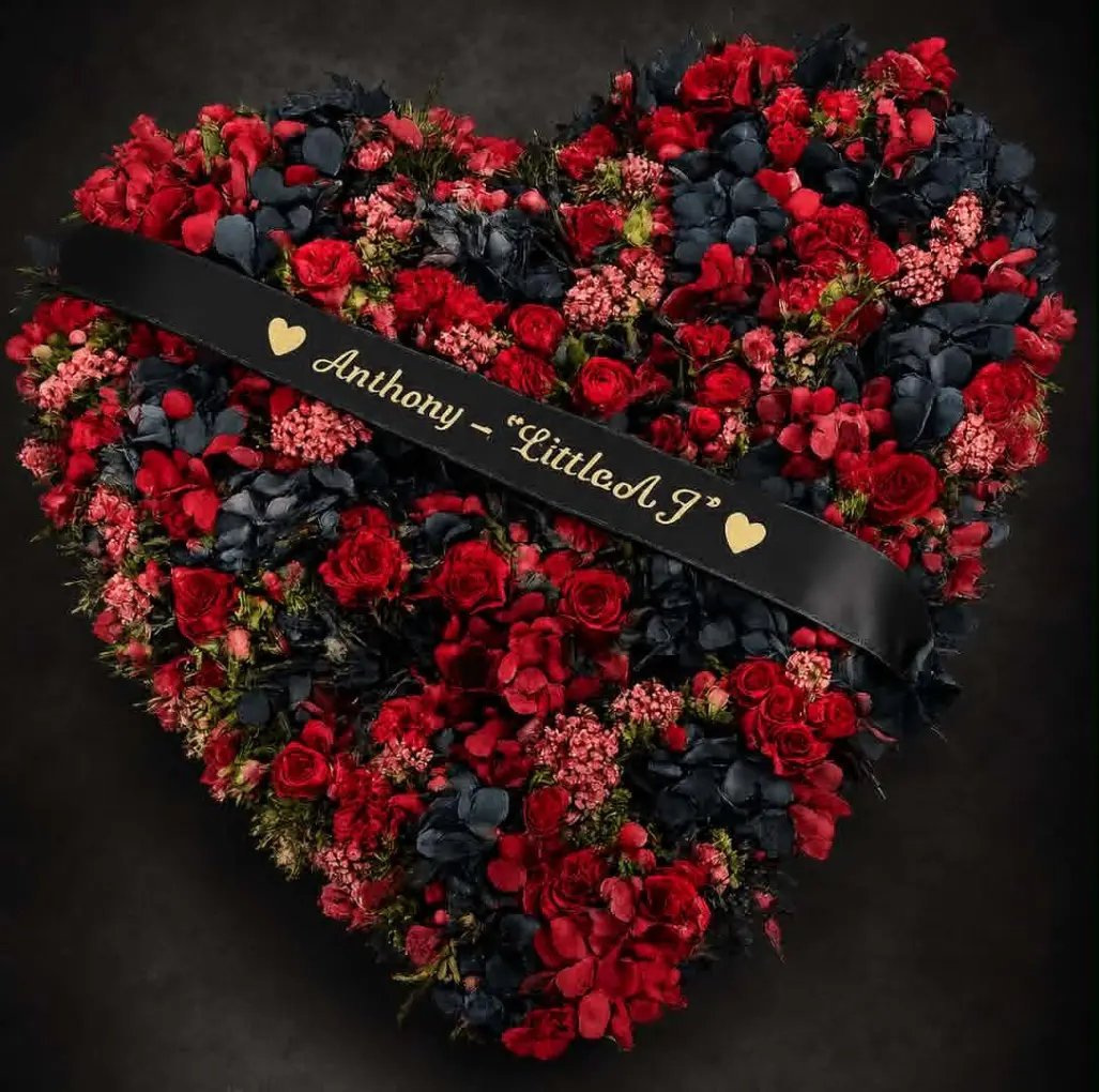 Heart-shaped funeral tribute featuring red roses, red flowers and dark foliage with a personalised ribbon, created as a meaningful floral tribute to honour a loved one.
